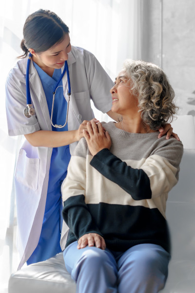 Female asian patient sitting and looking up to female doctor smiling standing by her side