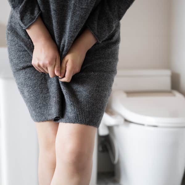 Woman standing in bathroom tightly crossing her legs implying she has to urinate