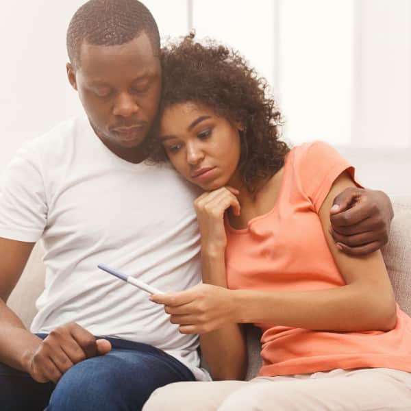 Couple embracing and appear somber while looking at pregnancy test
