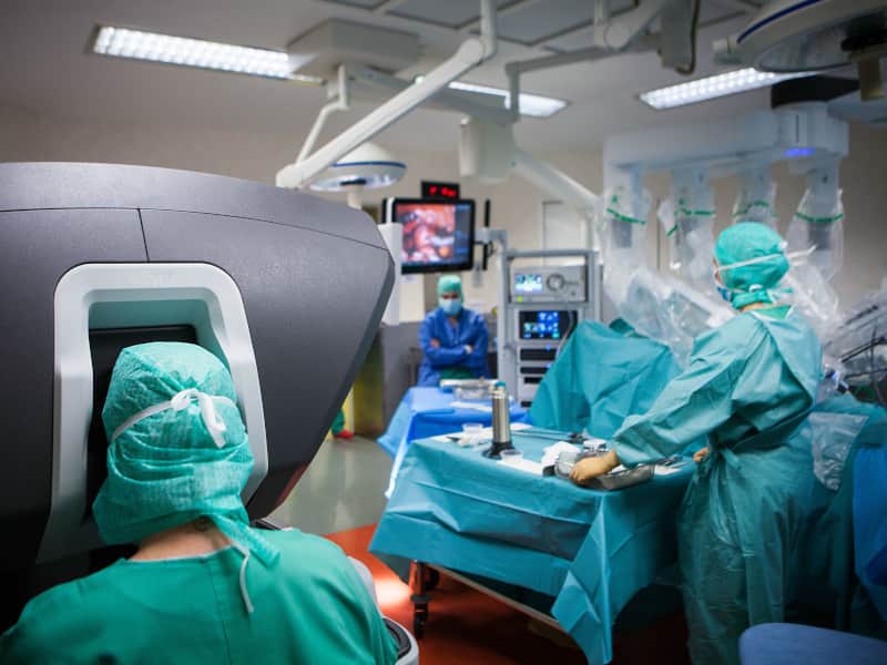 Doctor sitting at control panel performing robotic surgery in an operating room