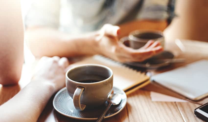 Close up of two womens hands next to their cups of coffee while having a discussion