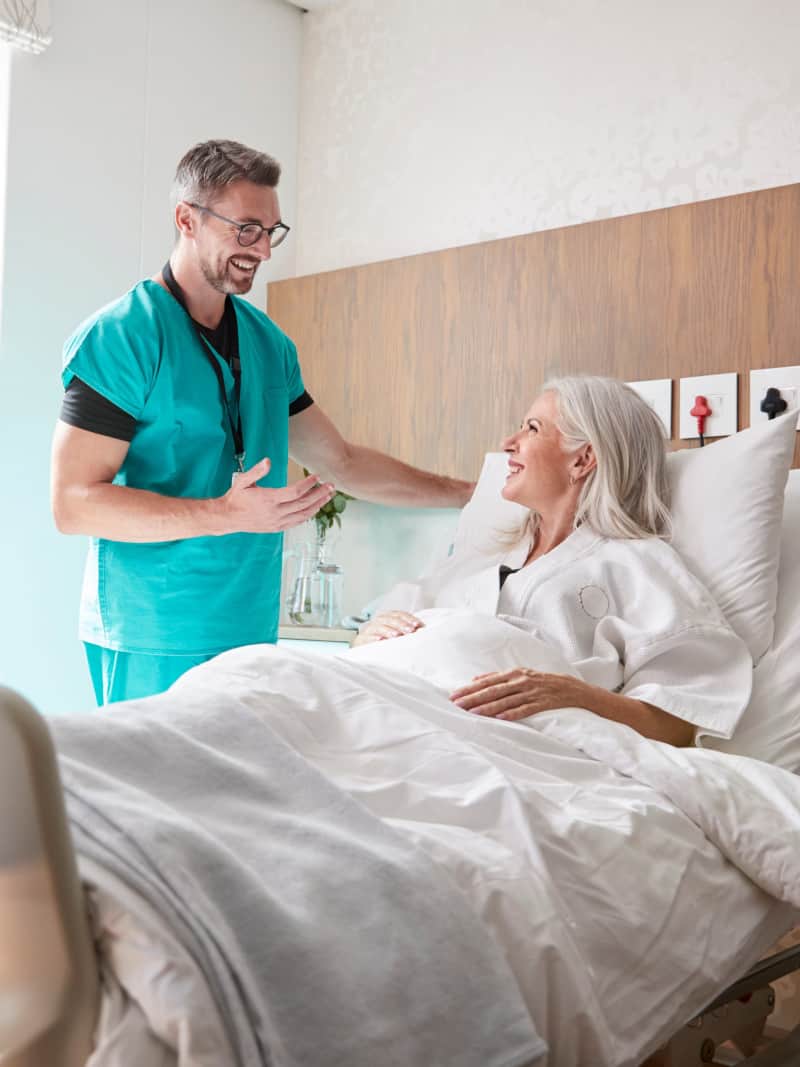 Surgeon Visiting And Talking With Female Patient In Hospital Bed