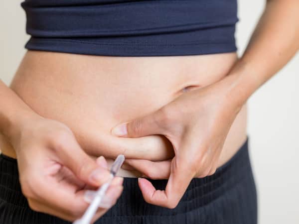 Closeup shot of a younger white female giving herself a hormone injection in the side of her abdomen