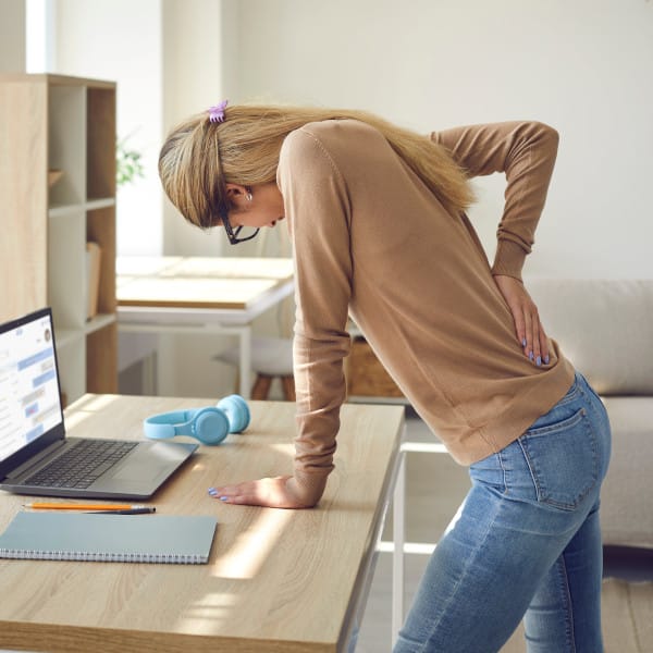 Woman standing at her desk in home holding her lower back due to pain