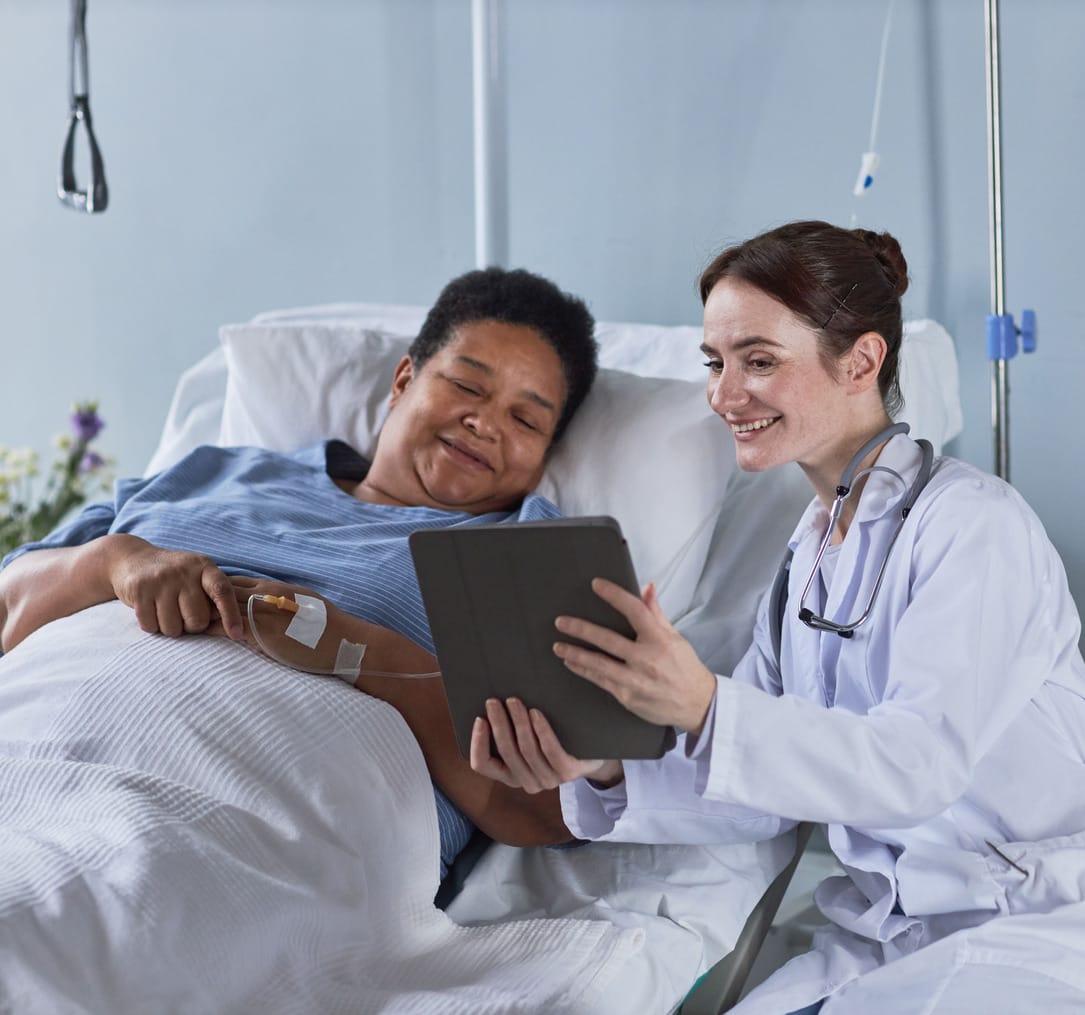Portrait of smiling young nurse showing digital tablet screen to senior African American woman in hospital bed 
