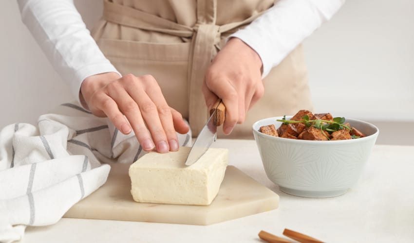 A woman cutting a block of tofu