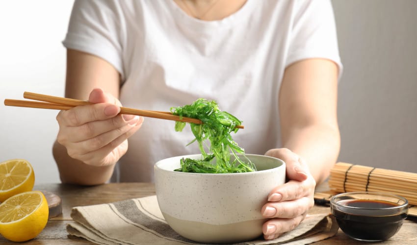 A white woman using chopsticks to pick up seaweed salad out of a bowl