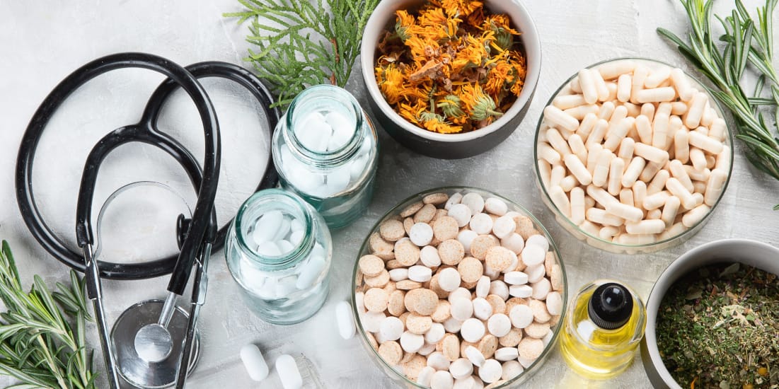 Top down view of various vitamins, herbs, and supplements, a stethoscope lay beside them
