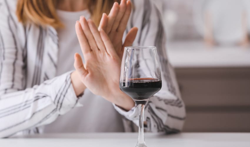 White woman with hands crossed saying no to glass of wine