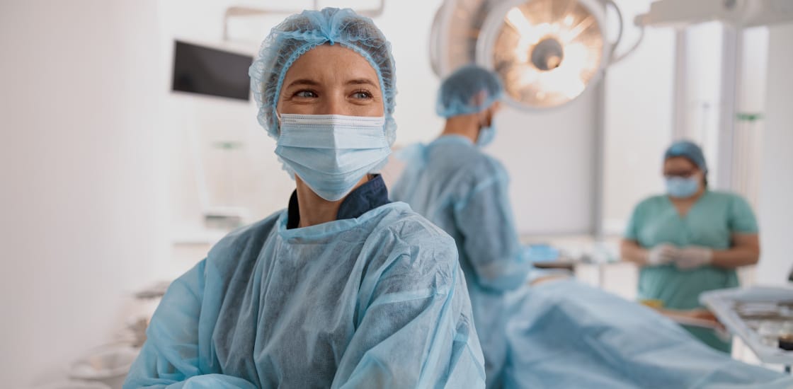 A female surgeon in scrubs in the OR confidently smiling as they perform surgery.