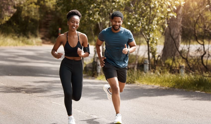 Smiling black woman running / exercising with black man on sunny mountain road