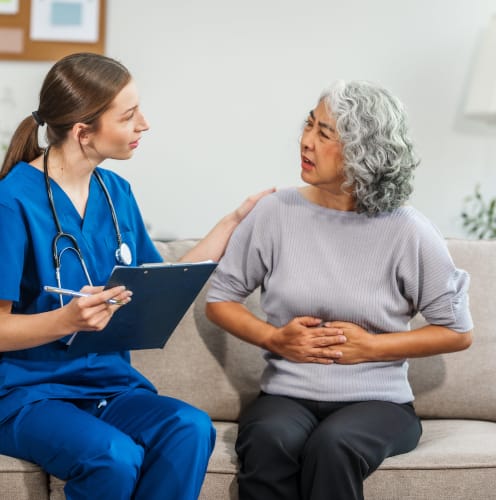 A young female physicians assistant empathizing and consulting with an older female patient, sitting on a couch
