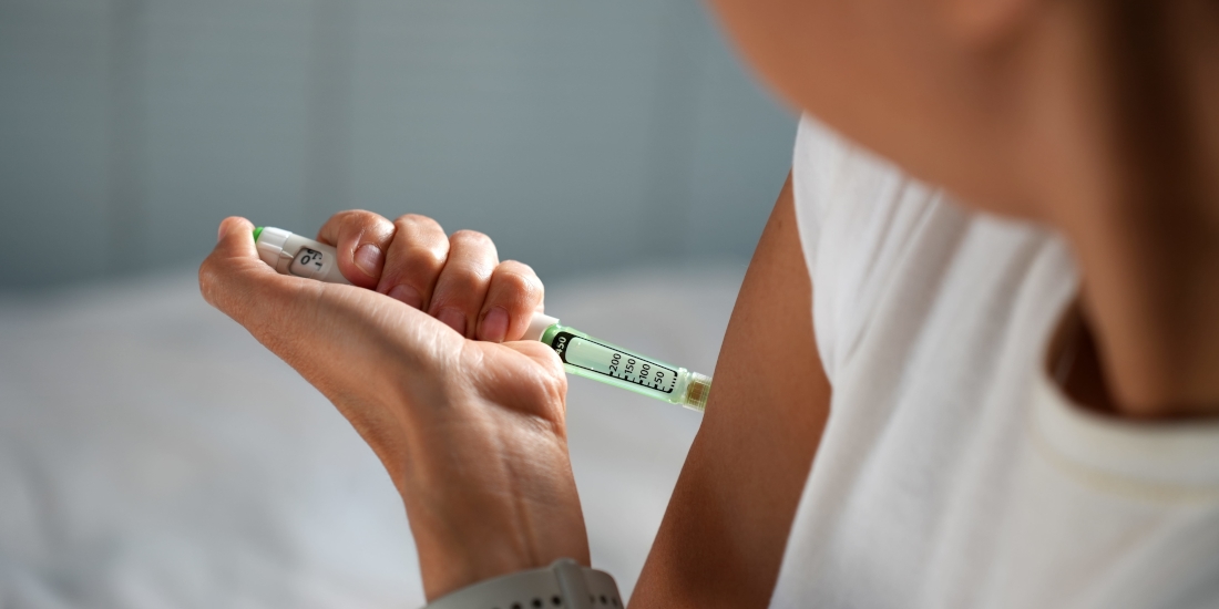 Close-up of woman injecting a hormonal therapy shot in shoulder with injection pen