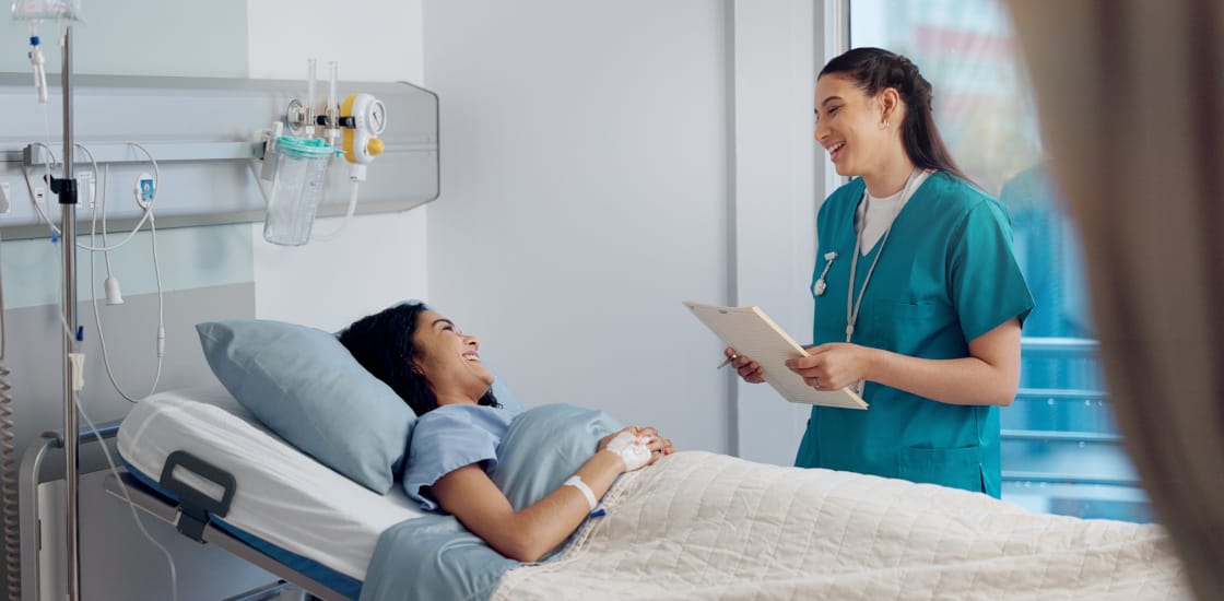 A young female smiling at a nurse while lying in a hospital bed.